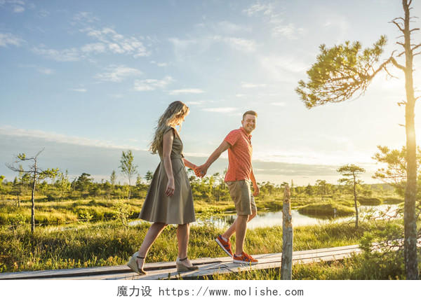 绿色植物和蓝天背景下行走在木桥上的情侣牵手幸福婚姻情侣幸福情侣幸福的人